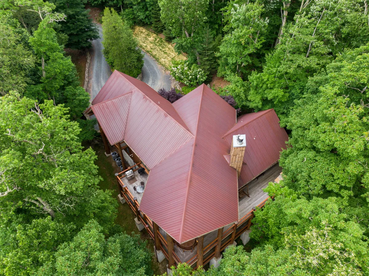 This exterior shot captures the unique architecture of Big Bear Lodge surrounded by lush greenery and a winding driveway. The house sits harmoniously within the natural landscape, inviting guests to embark on outdoor adventures right from the doorstep. The expansive deck is visible, hinting at outdoor relaxation and gatherings.