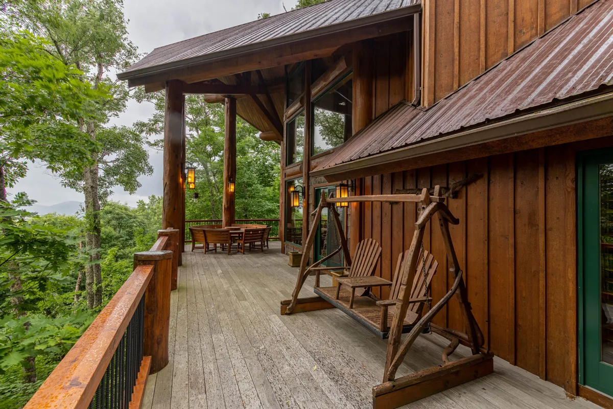 This exterior scene features a wooden swing and outdoor dining table on a deck with large windows and wooden beams, all overlooking a natural, leafy landscape. The peaceful, open-air space provides an ideal spot to unwind with a pet after an adventure.