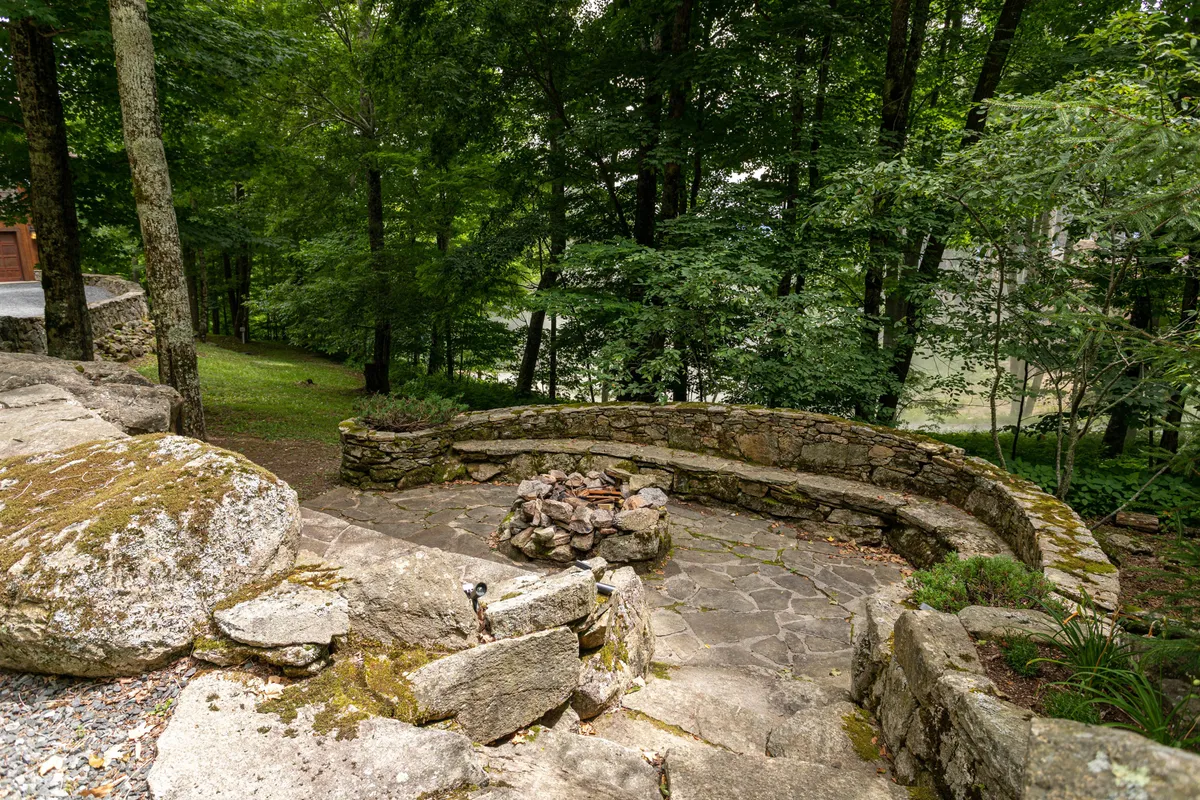 A beautifully crafted stone fire pit is surrounded by a stone seating area nestled amongst tall trees. The space feels both intimate and evocative of a national park, inviting guests to gather, share stories, and stargaze under the open sky.