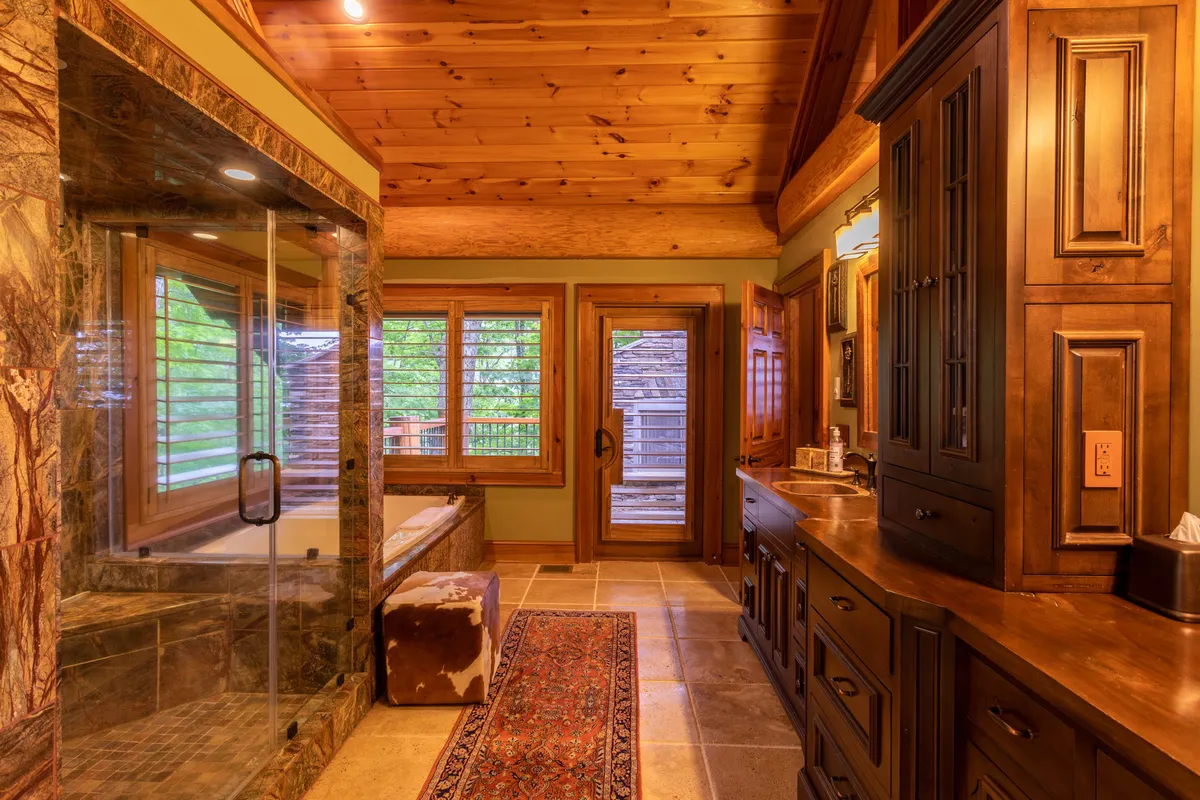 A luxurious spa-inspired bathroom featuring a glass shower, a bathtub beside wooden cabinetry, and windows streaming in natural light. The space feels airy and peaceful, perfect for unwinding after a day in the mountains.