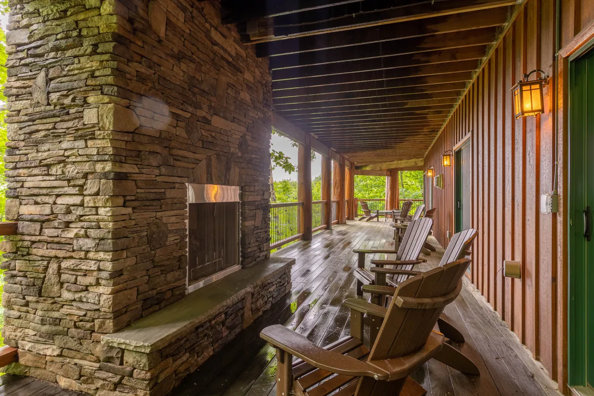 An inviting outdoor space with a stone fireplace, Adirondack chairs, and green foliage surrounding the wooden deck. This area is perfect for gathering, socializing, and sharing stories by the fire pit as the day ends.